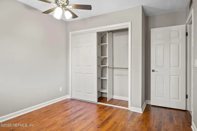 an empty room with wooden floor closet fan and windows