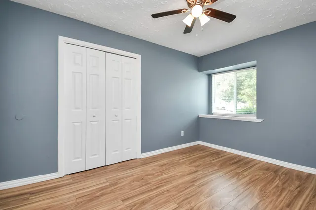 an empty room with wooden floor chandelier fan and windows