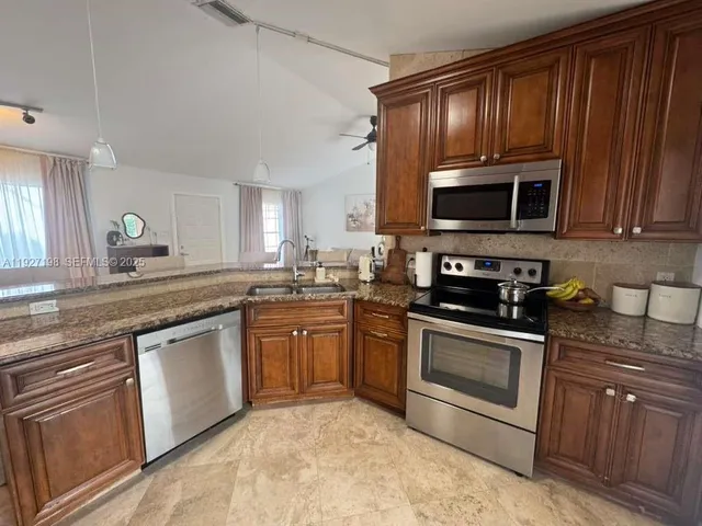 a kitchen with granite countertop wooden cabinets stainless steel appliances and a sink