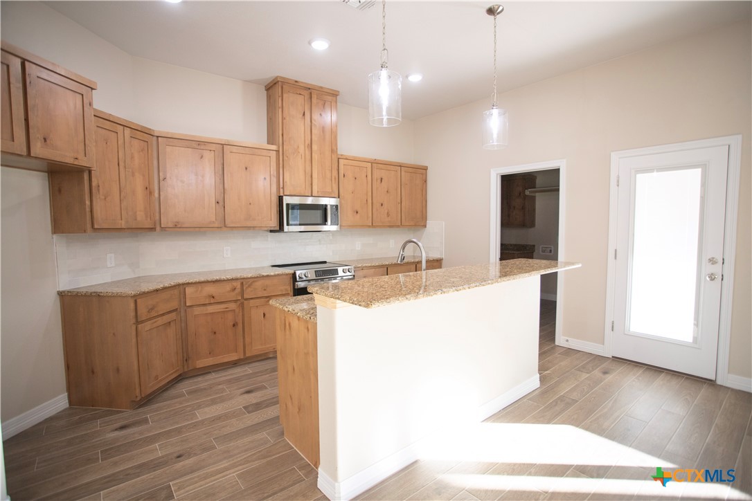 3213 Digby Drive Belton, TX 76513 - Photo 4 of 18 a kitchen with kitchen island granite countertop wooden floors white cabinets and stainless steel appliances