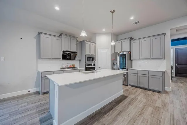 a large kitchen with kitchen island a sink dishwasher a stove a refrigerator and white cabinets with wooden floor