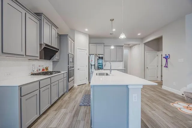 a large kitchen with stainless steel appliances kitchen island a sink dishwasher a refrigerator and a oven with wooden floor