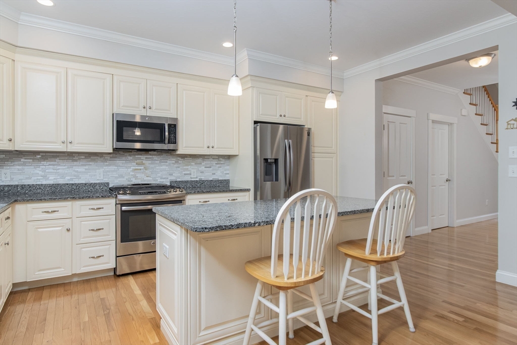 21 A Blacksmith Row, Unit 21 Groton, MA 01450 - Photo 8 of 42 a kitchen with stainless steel appliances granite countertop a dining table chairs refrigerator and microwave