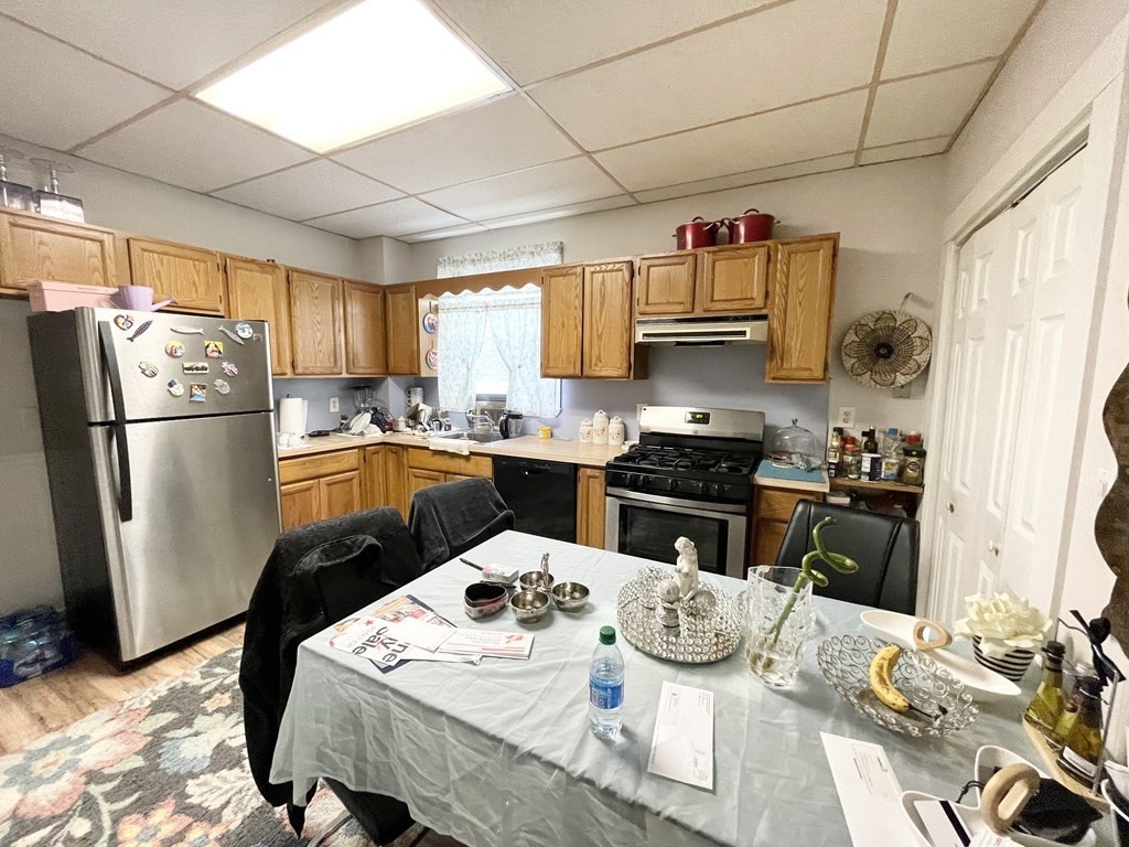 a kitchen with stainless steel appliances granite countertop a refrigerator a sink dishwasher a stove a dining table and chairs with wooden floor