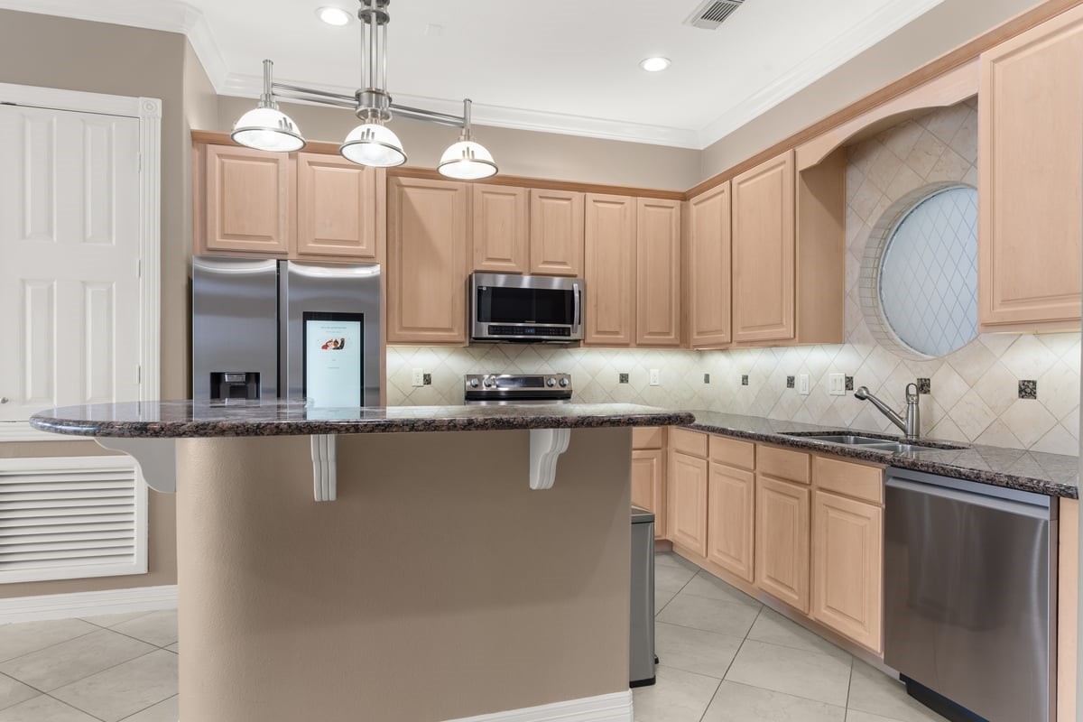 168 Lake Point Boulevard, Unit C102 Conroe, TX 77356 - Photo 9 of 35 This modern kitchen features light wood cabinetry, stainless steel appliances, and granite countertops. It includes a stylish breakfast bar, tiled backsplash, and a circular window adding charm and natural light. Perfect for entertaining and everyday living.