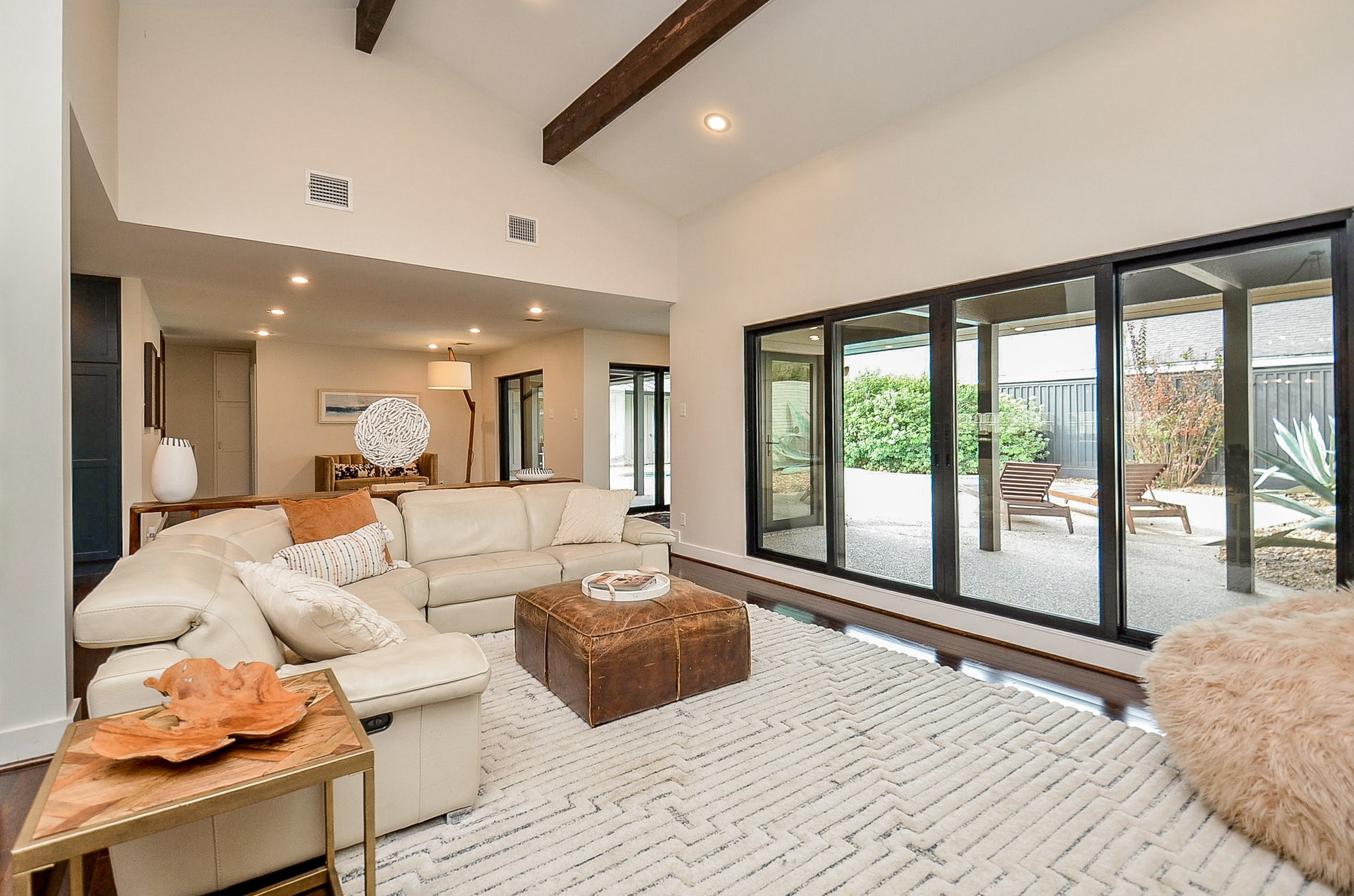 10003 Burgoyne Road Houston, TX 77042 - Photo 10 of 48 Spacious living area with vaulted, beamed ceilings and expansive glass sliders that open directly to the pool and courtyard. The open layout enhances flow between indoor and outdoor spaces, while natural light and clean lines highlight the home’s architectural beauty.