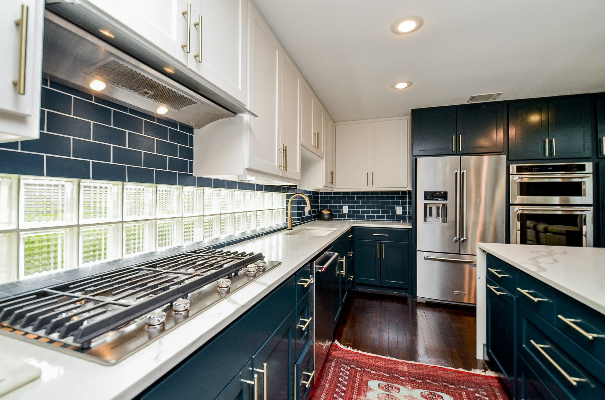 10003 Burgoyne Road Houston, TX 77042 - Photo 16 of 48 A cook's delight, imagine cooking here! This professionally designed kitchen offers generous counter space and abundant storage, with a combination of white and navy cabinetry creating a clean, functional layout. Glass block windows introduce natural light, while the gold faucet and blue tile backsplash add a polished, modern finish