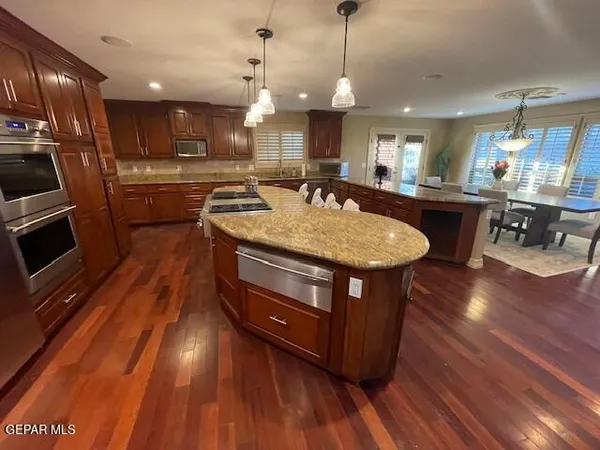 a kitchen with stainless steel appliances granite countertop a stove a sink dishwasher a microwave oven and a dining table with wooden floor