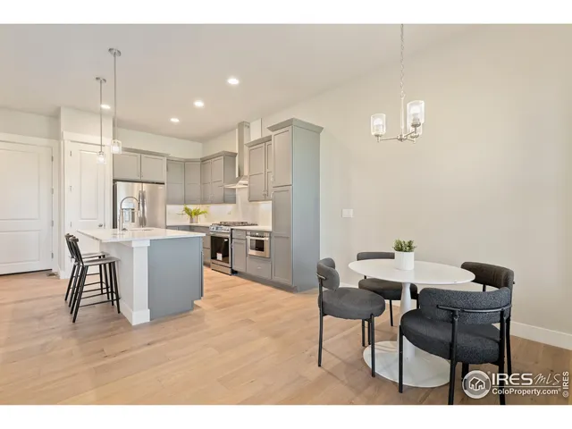 a open kitchen with stainless steel appliances kitchen island granite countertop a dining table chairs and a refrigerator