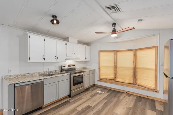 a kitchen with stainless steel appliances granite countertop a stove a sink and white cabinets with wooden floor