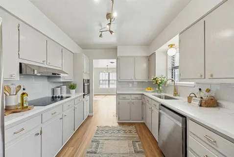 a kitchen with stainless steel appliances granite countertop a sink dishwasher a stove and white cabinets with wooden floor