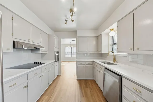 a kitchen with stainless steel appliances granite countertop a sink dishwasher a stove and white cabinets with wooden floor