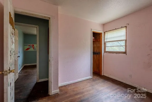 an empty room with wooden floor closet and windows
