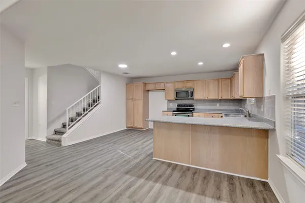 a kitchen with stainless steel appliances granite countertop a sink a stove top oven a refrigerator with grey cabinets and wooden floor