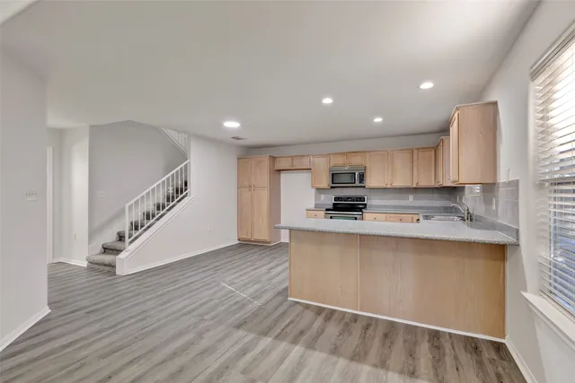 a kitchen with stainless steel appliances granite countertop a sink a stove top oven a refrigerator with grey cabinets and wooden floor