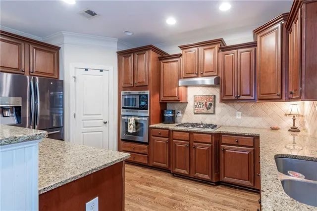 a kitchen with stainless steel appliances granite countertop wooden cabinets a sink and dishwasher a stove with wooden floor