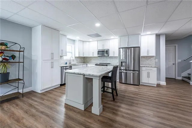 a kitchen with stainless steel appliances a refrigerator a sink dishwasher a stove a refrigerator and white cabinets with wooden floor