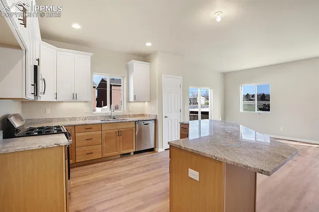 a kitchen with stainless steel appliances granite countertop a kitchen island a stove a sink a refrigerator and white cabinets with wooden floor