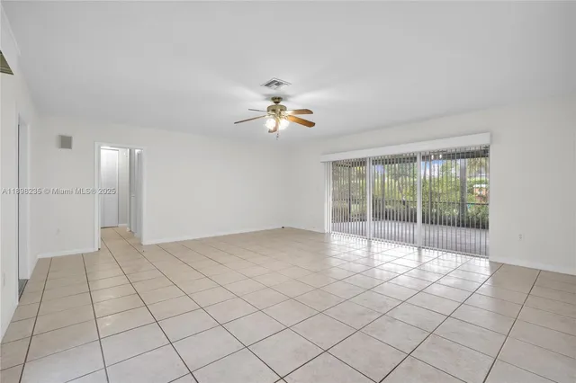 a view of an empty room and chandelier fan and kitchen view