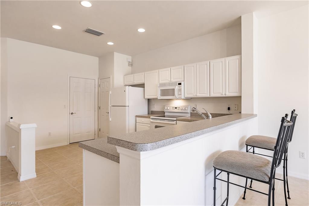 15451 Marcello Circle, Unit 229 Naples, FL 34110 - Photo 5 of 30 a kitchen with a sink a stove a refrigerator and white cabinets