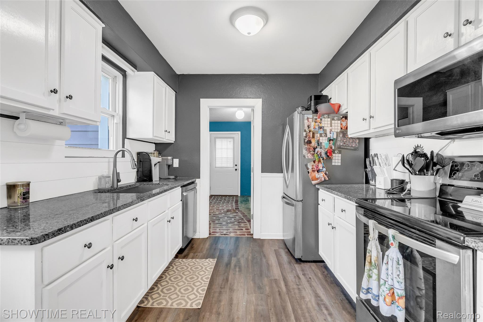 3444 Maple Street Port Huron, MI 48060 - Photo 11 of 30 Galley kitchen featuring white cabinetry, dark granite-style countertops, wood-finish flooring, a stainless steel refrigerator, and a built-in microwave