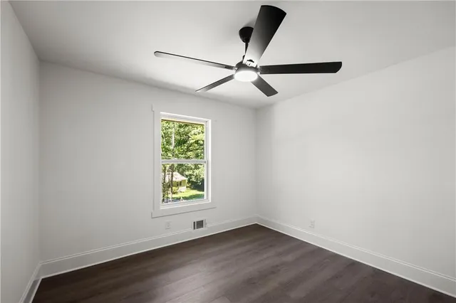 an empty room with wooden floor ceiling fan and windows