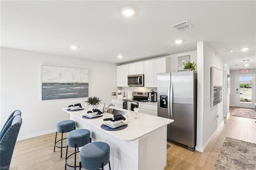 8052 Cedar Ky Way Lehigh Acres, FL 33971 - Photo 13 of 45 Model home. Kitchen featuring stainless steel appliances, a kitchen breakfast bar, a center island with sink, white cabinetry, and recessed lighting