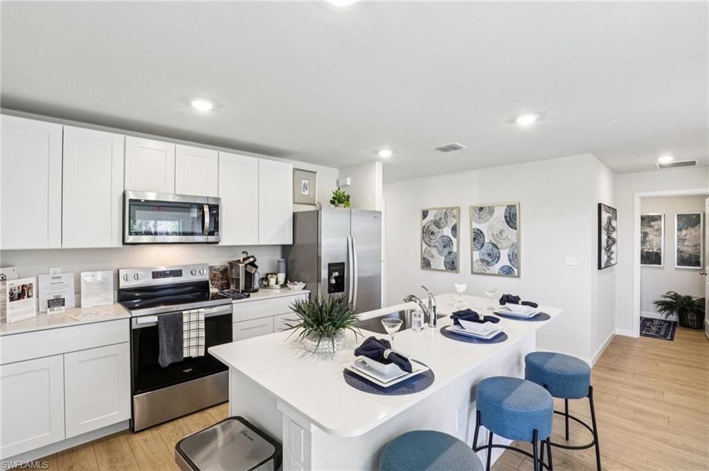 8052 Cedar Ky Way Lehigh Acres, FL 33971 - Photo 15 of 45 Model home. Kitchen with stainless steel appliances, a breakfast bar, light wood-style floors, an island with sink, and recessed lighting