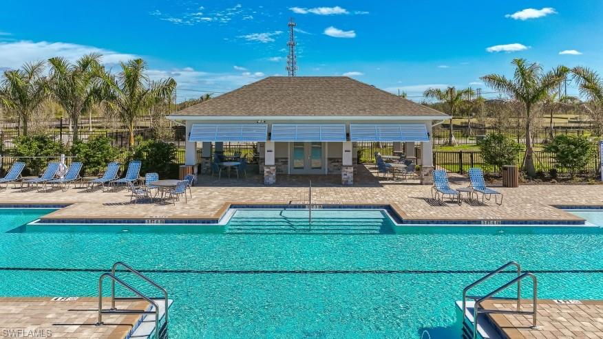 8052 Cedar Ky Way Lehigh Acres, FL 33971 - Photo 40 of 45 A spacious swimming pool area featuring a shaded pavilion, sun loungers, and palm trees, all set against a clear blue sky