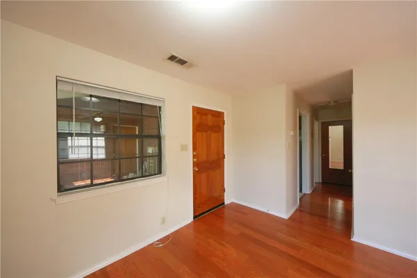 a view of an empty room with wooden floor and a window