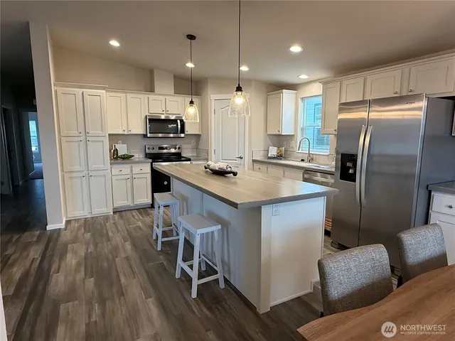 a kitchen with stainless steel appliances granite countertop a refrigerator a sink dishwasher a stove with white cabinets and wooden floor