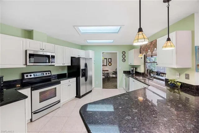 a large kitchen with stainless steel appliances granite countertop a stove a sink dishwasher a refrigerator white cabinets and wooden floor