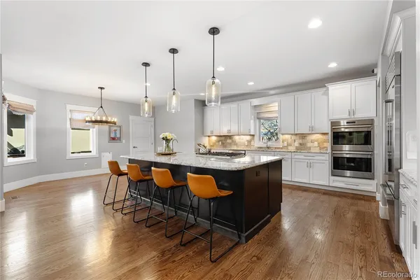 a open kitchen with stainless steel appliances granite countertop a stove top oven a refrigerator a sink and a dining table with wooden floor