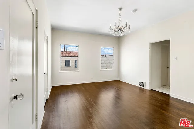 an empty room with wooden floor chandelier and windows