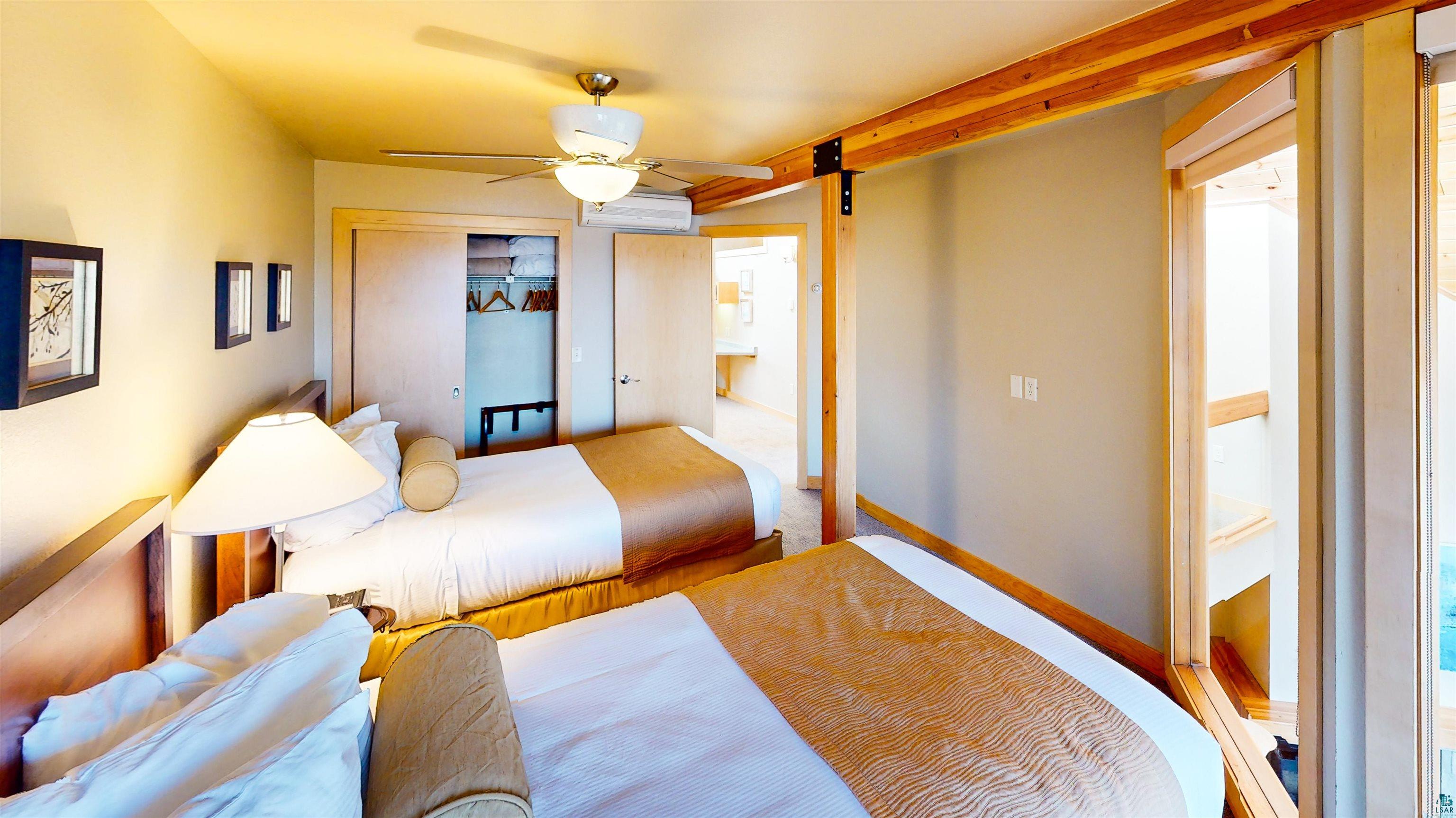 40 Surfside Drive, Unit 5D Tofte, MN 55615 - Photo 36 of 37 Interior bedroom featuring exposed wood ceiling beams and trim, a ceiling fan with integrated lighting, a built-in closet with sliding wood doors, and wood-finish flooring