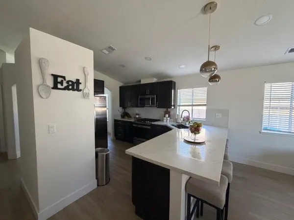 a kitchen with stainless steel appliances granite countertop a sink a refrigerator a stove a microwave oven a dining table and chairs with wooden floor