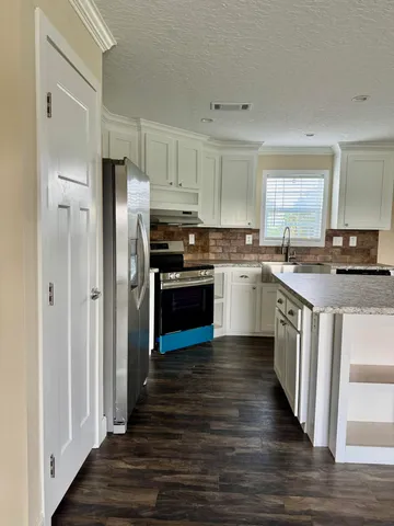 a kitchen with stainless steel appliances granite countertop a stove top oven a refrigerator and a granite counter tops with wooden floors