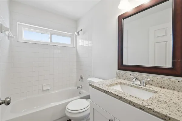a bathroom with a granite countertop sink a mirror a toilet and bathtub