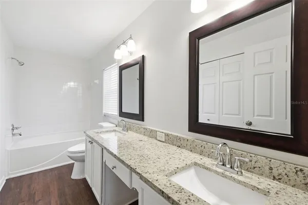 a bathroom with a granite countertop double vanity sink mirror and a bathtub