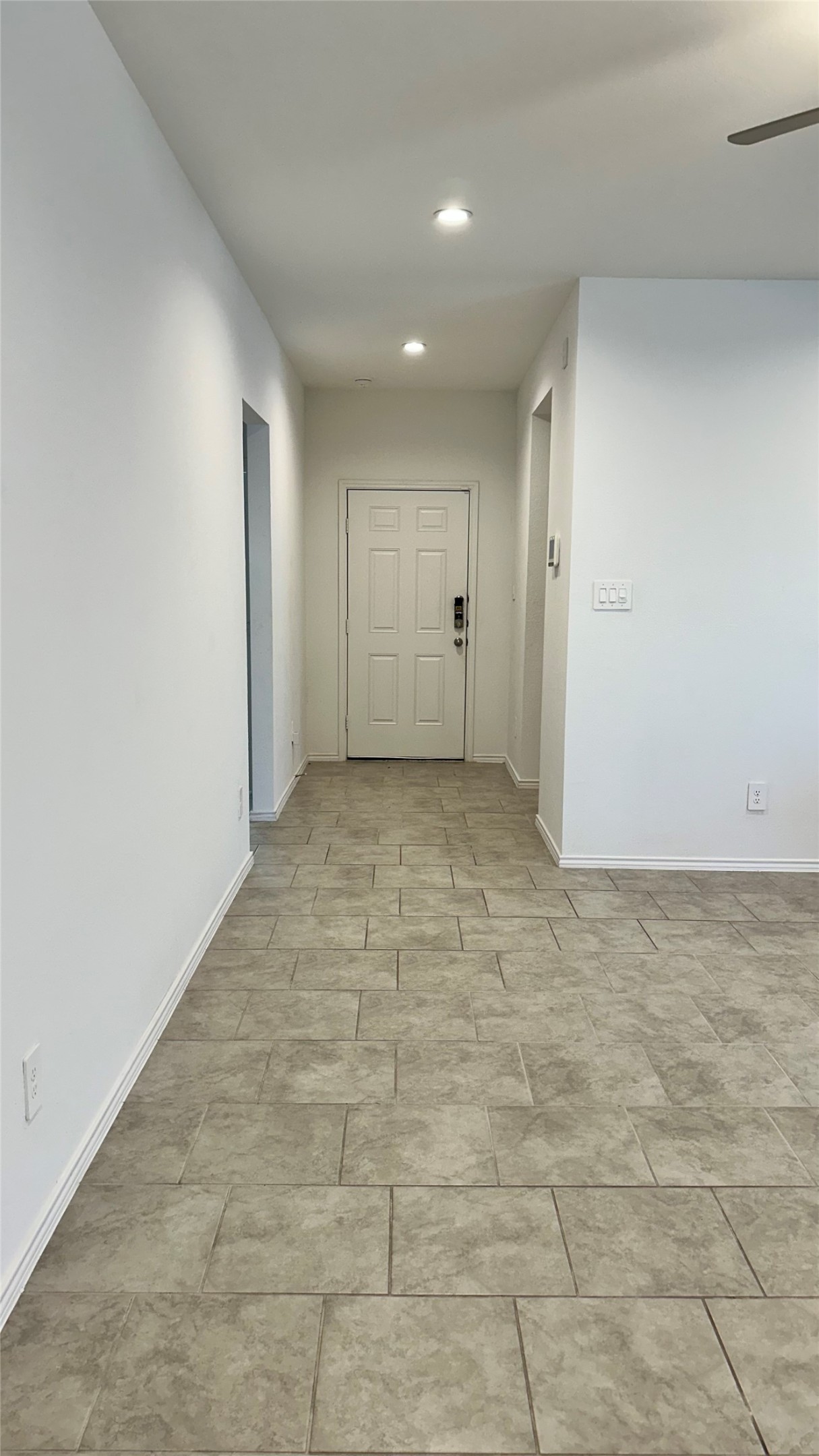 1103 Cattle Chute Court Rosharon, TX 77583 - Photo 3 of 26 This photo shows a modern, well-lit hallway with light gray tiled flooring and white walls, leading to a white door. Recessed ceiling lights add to the clean and spacious feel.