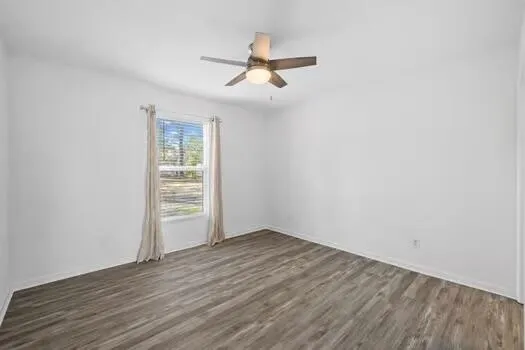an empty room with wooden floor chandelier fan and windows