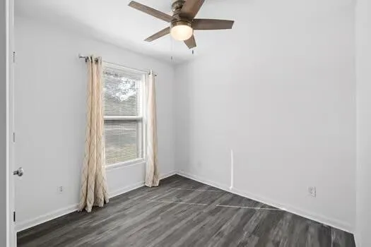 an empty room with wooden floor fan and windows