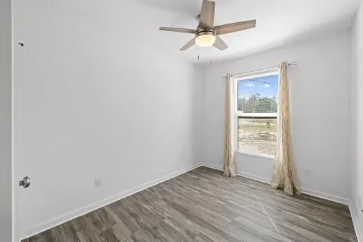 an empty room with wooden floor fan and windows