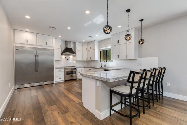 a kitchen with stainless steel appliances granite countertop a sink a stove a refrigerator and island with wooden floor