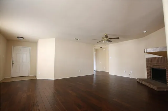 an empty room with wooden floor fireplace and windows