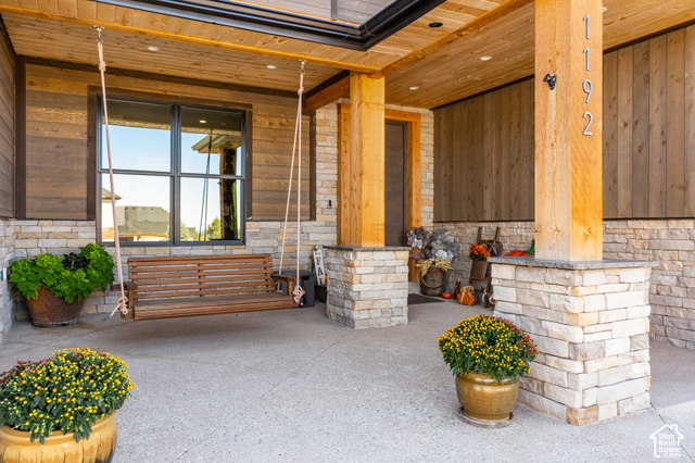 1192 East Ashdown Road Cedar City, UT 84721 - Photo 22 of 96 Covered patio with stone and wood-finish siding, exposed wood ceiling, a large window, and a wood porch swing