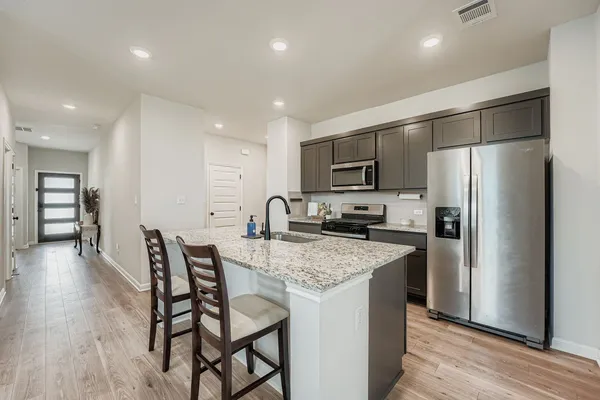 a kitchen with stainless steel appliances granite countertop a refrigerator a stove top oven a sink dishwasher a dining table and chairs with wooden floor