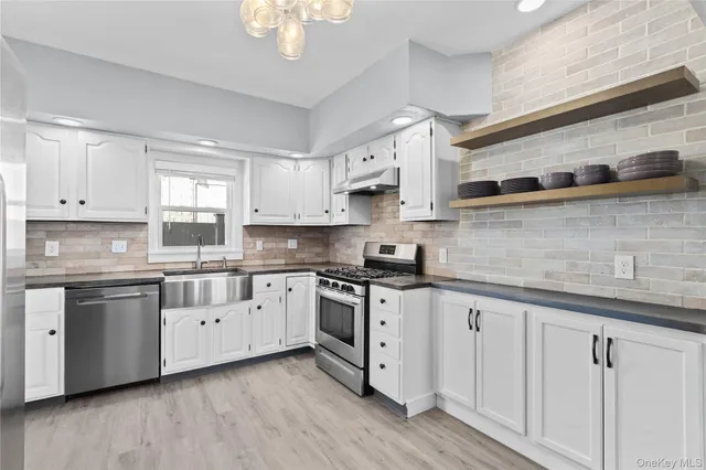 a kitchen with stainless steel appliances granite countertop white cabinets a sink a stove a dining table and chairs