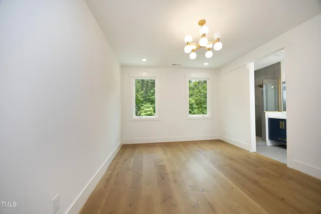 an empty room with wooden floor chandelier and windows