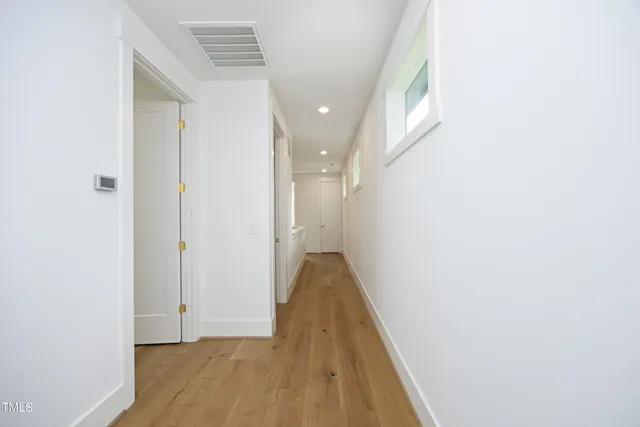a view of a hallway with wooden floor and a bathroom